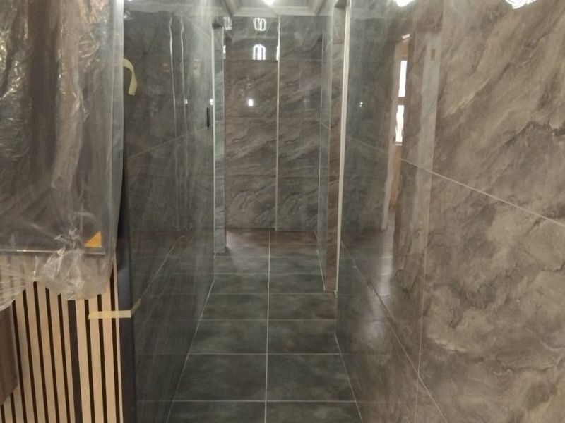 A modern hallway featuring high-gloss marble-effect wall tiles, large format floor tiles, and decorative ceiling detailing with integrated lighting.