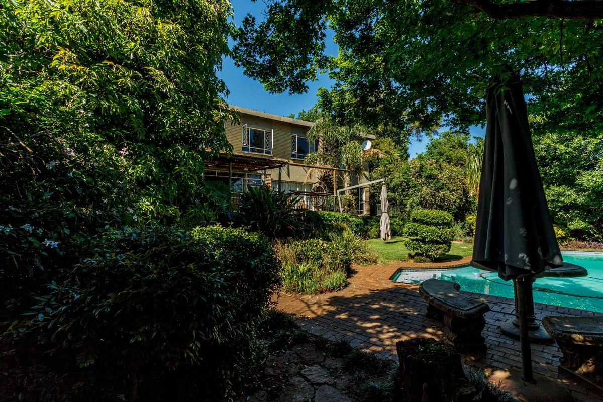 A lush rear garden featuring a swimming pool, brick paved patio area, and mature landscaping surrounding the back elevation of the house.
