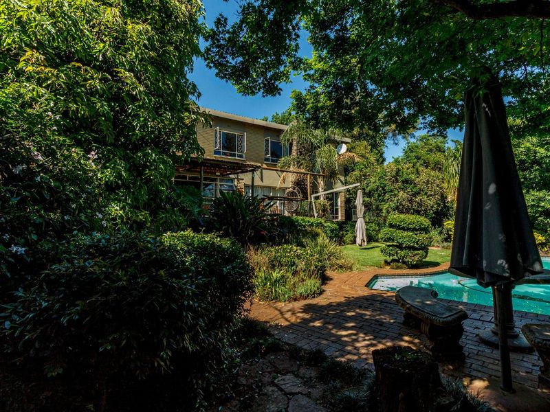 A lush rear garden featuring a swimming pool, brick paved patio area, and mature landscaping surrounding the back elevation of the house.