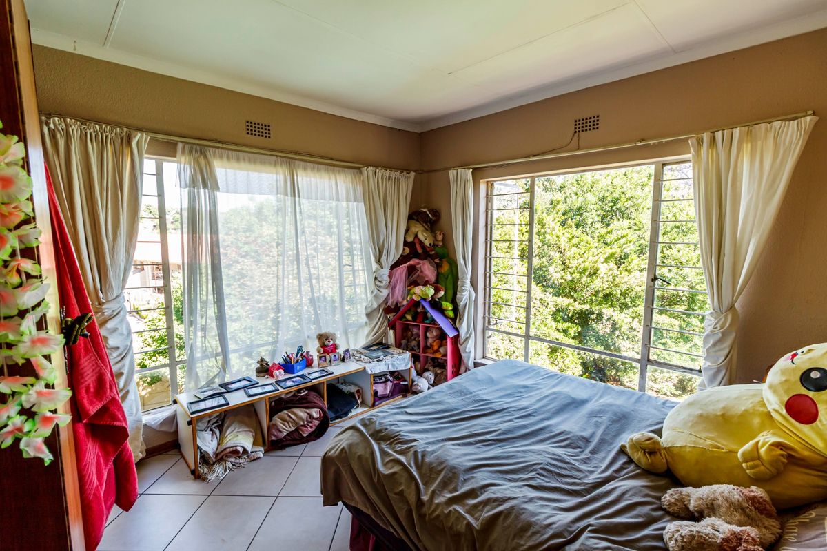 A bedroom featuring large windows that provide ample natural light, tiled flooring, and neutral wall tones, offering a functional space with potential for modernization.