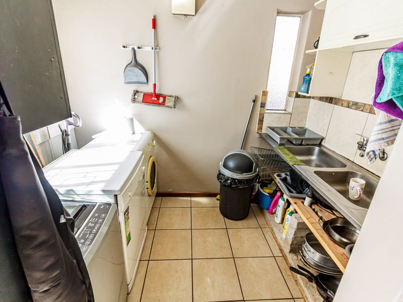 A functional laundry area featuring a double stainless steel sink, tiled splashback, and tiled flooring with open shelving for storage.