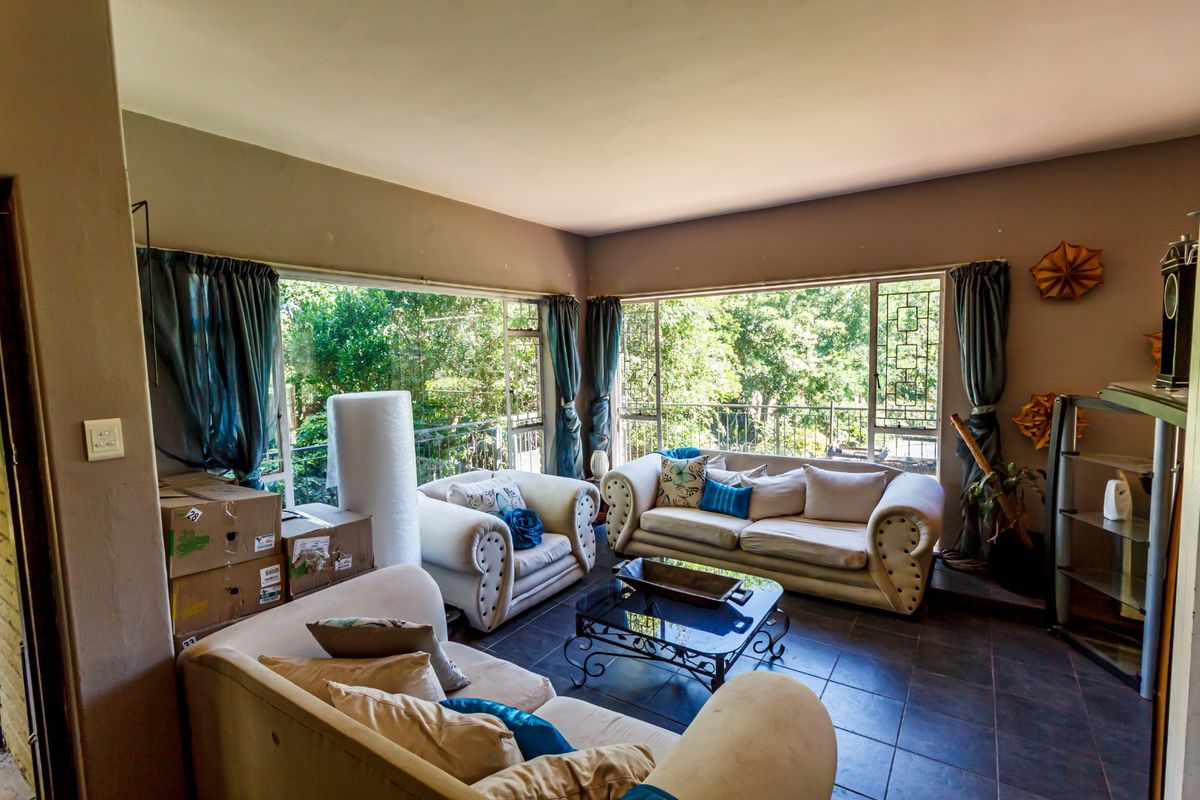 Spacious living room featuring large corner windows that provide ample natural light and views of the surrounding greenery, complemented by dark tiled flooring.