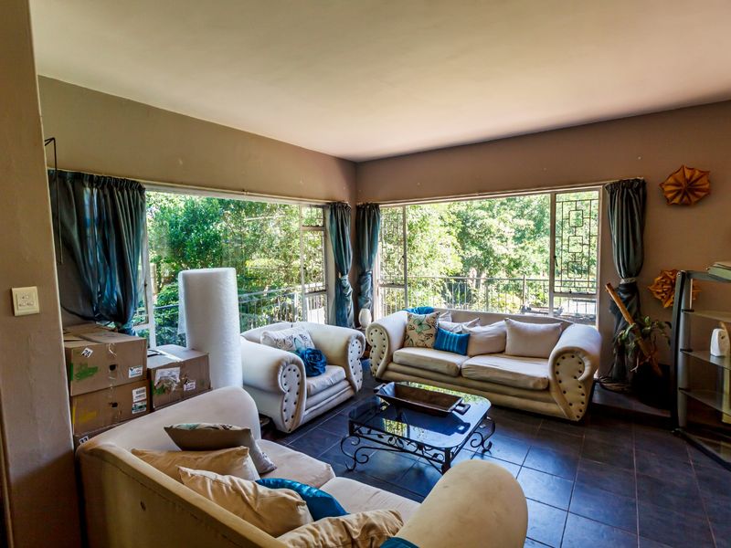 Spacious living room featuring large corner windows that provide ample natural light and views of the surrounding greenery, complemented by dark tiled flooring.