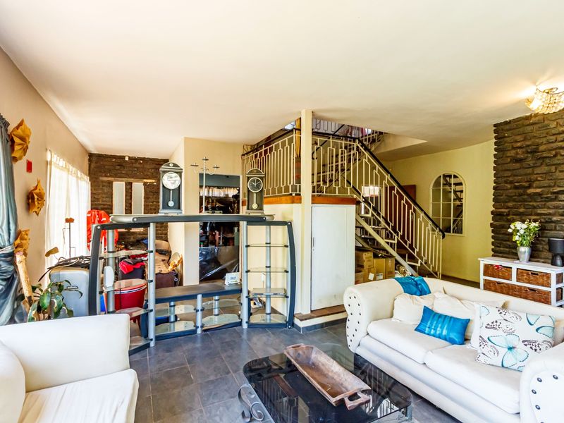 Spacious living area featuring exposed brick walls, tiled flooring, and an open staircase with decorative metal railings.