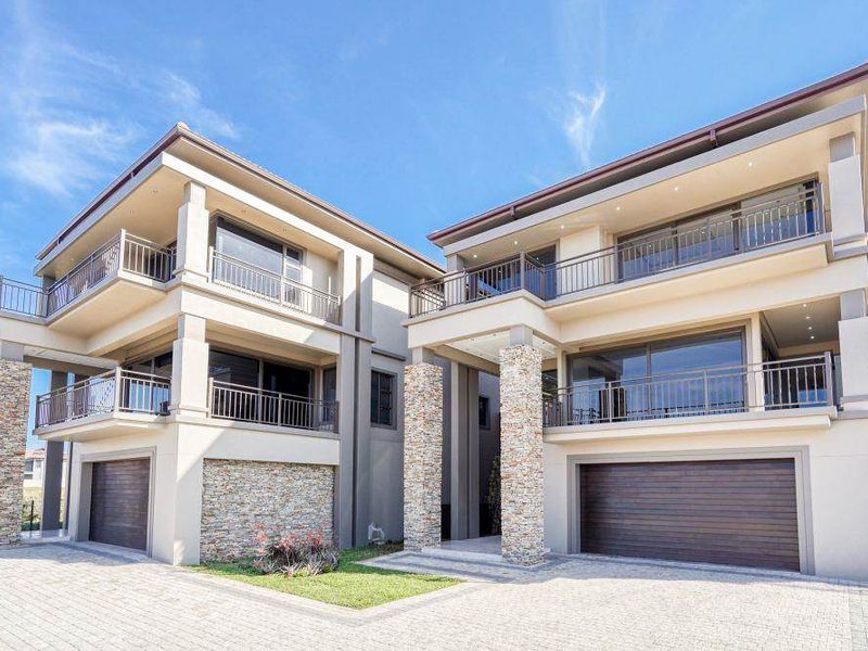 Modern multi-story apartment complex featuring stone-clad pillars, spacious balconies with metal railings, and integrated double garages with a paved driveway.