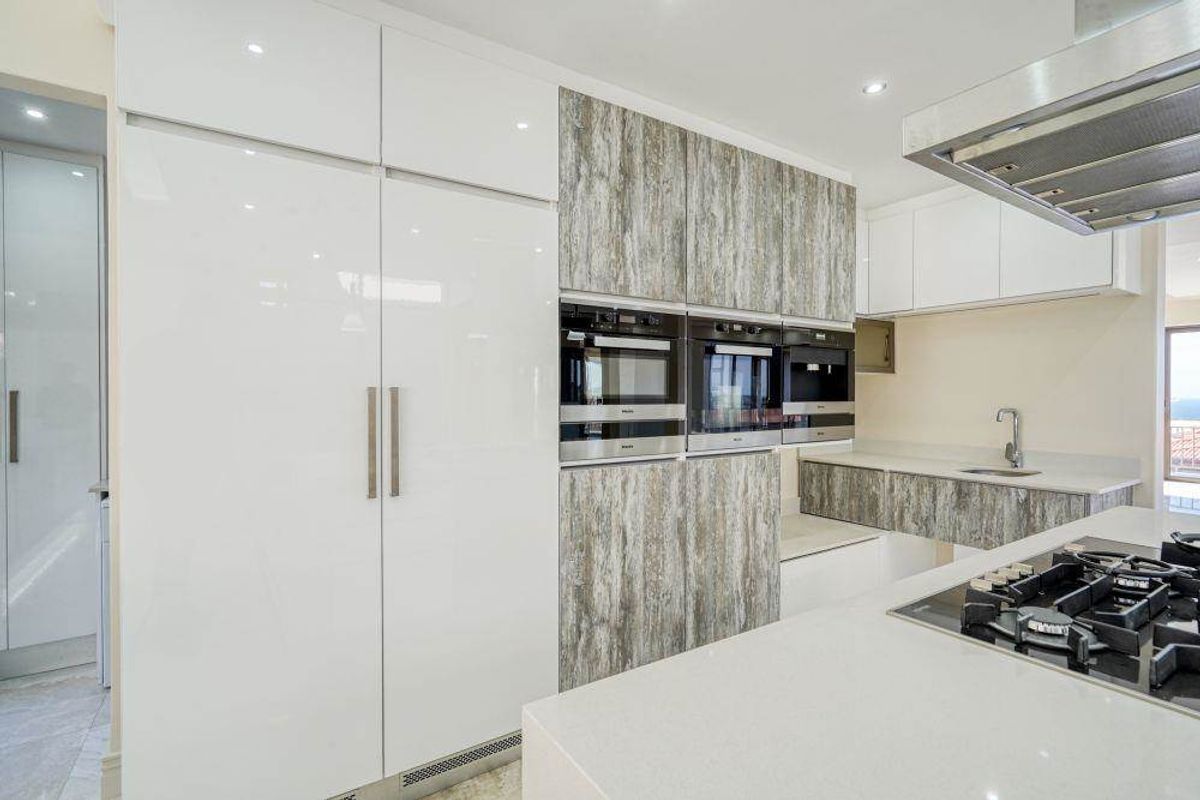 Modern kitchen featuring high-gloss cabinetry, integrated appliances, built-in ovens, gas cooktop, and stone countertops with a sleek, contemporary finish.