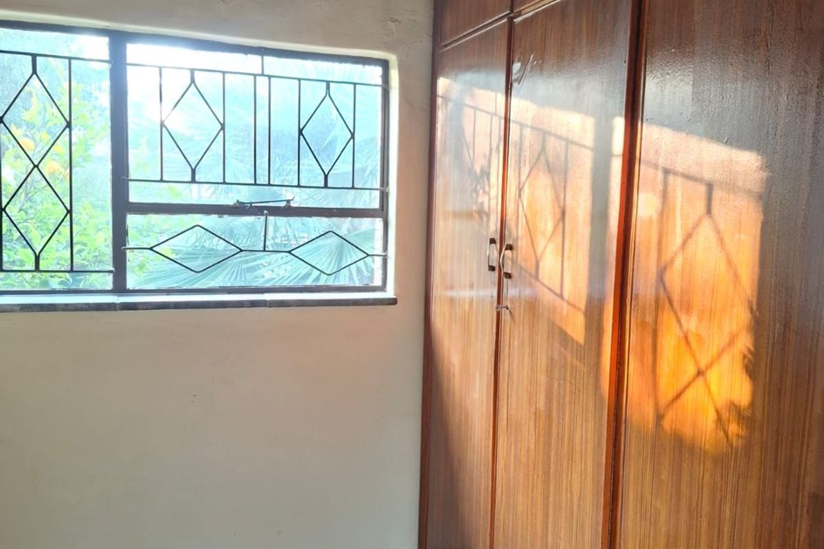 A bedroom featuring built-in wooden cupboards, carpeted flooring, and security burglar bars on the window.