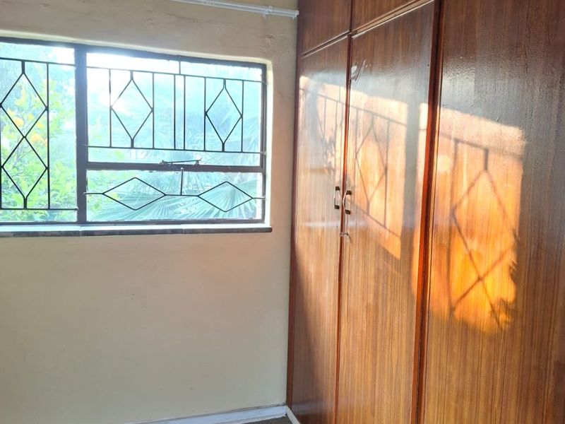 A bedroom featuring built-in wooden cupboards, carpeted flooring, and security burglar bars on the window.