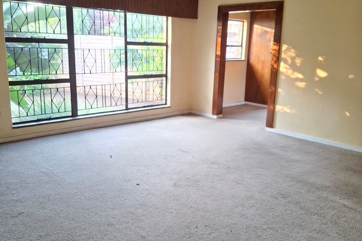 Spacious living area featuring neutral walls, carpeted flooring, a ceiling fan, and large windows with security bars, offering a blank canvas for interior design.