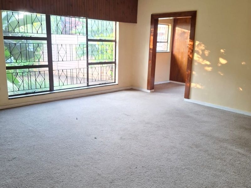 Spacious living area featuring neutral walls, carpeted flooring, a ceiling fan, and large windows with security bars, offering a blank canvas for interior design.