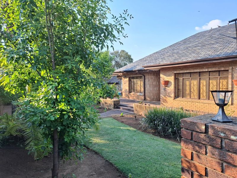 A well-maintained rear exterior view of a brick house featuring a paved patio area, landscaped garden, and secure window treatments.