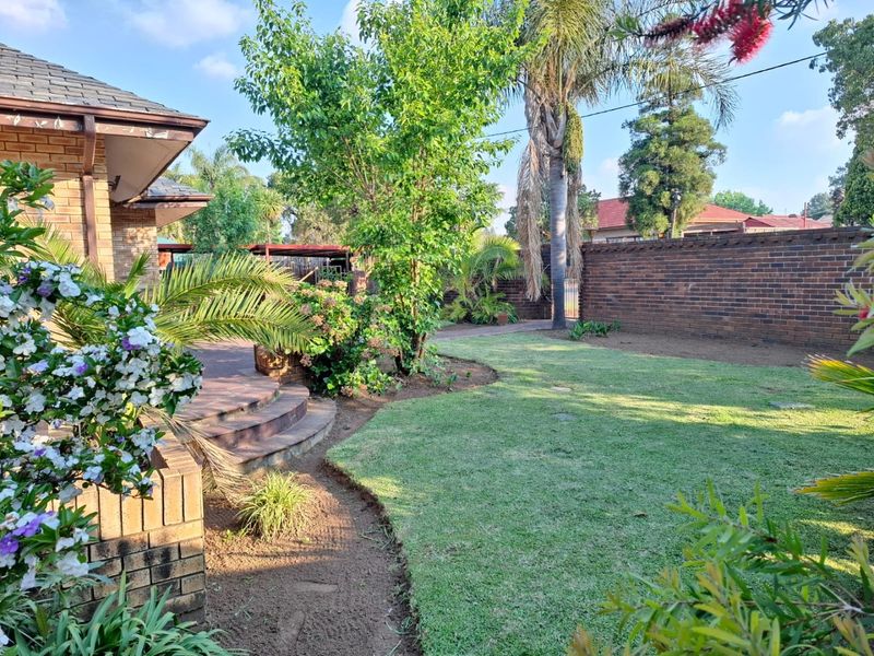 A well-maintained rear garden featuring a paved patio area, brick boundary wall, and established landscaping with a lawn.