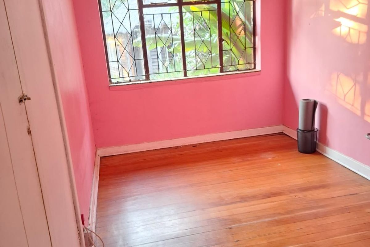 An empty bedroom featuring original timber flooring, built-in cupboard storage, and security bars on the window.