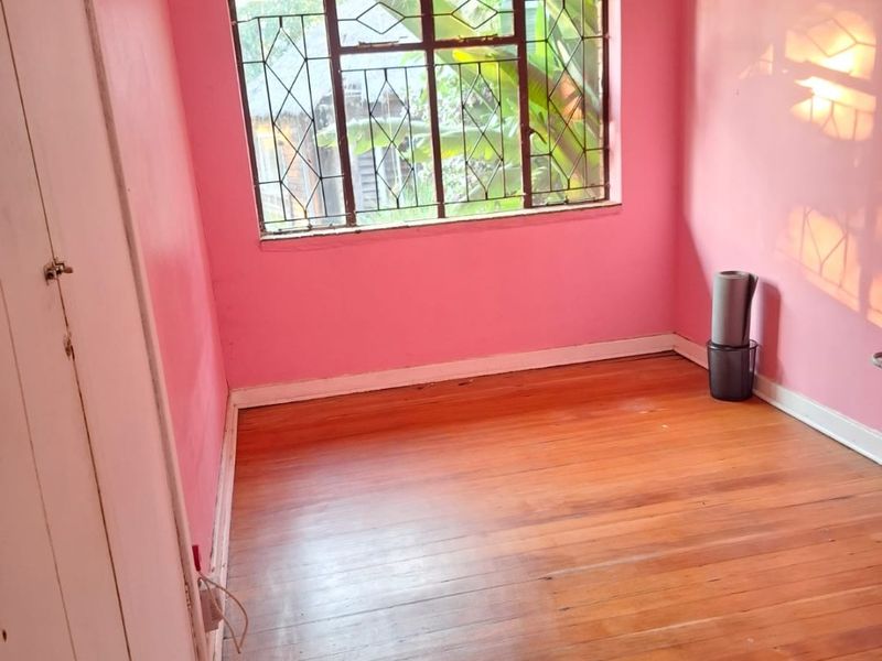 An empty bedroom featuring original timber flooring, built-in cupboard storage, and security bars on the window.
