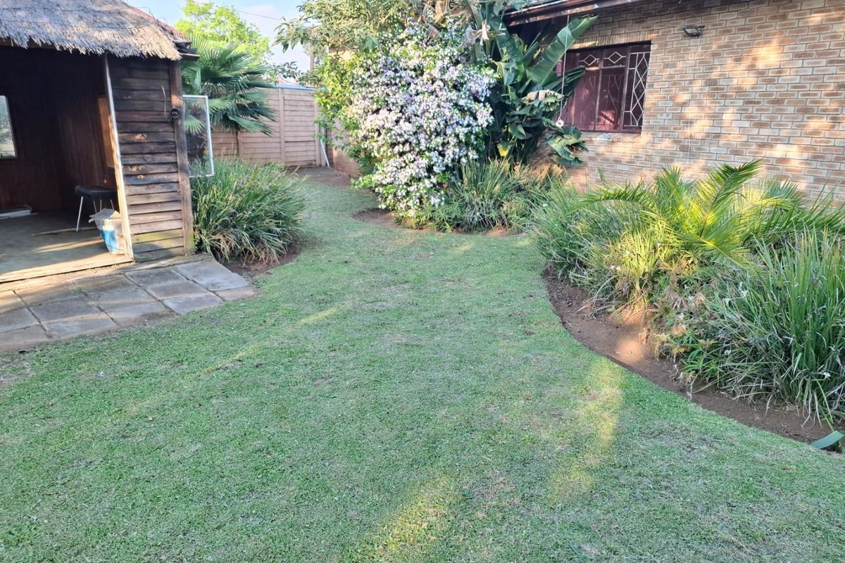 A private rear garden featuring a thatched lapa, paved patio area, and established garden beds adjacent to the main brick residence.