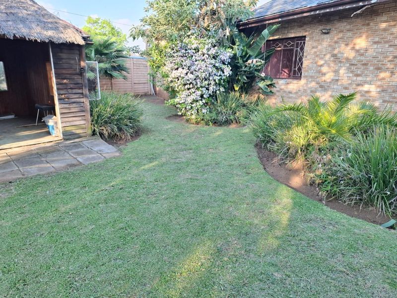 A private rear garden featuring a thatched lapa, paved patio area, and established garden beds adjacent to the main brick residence.