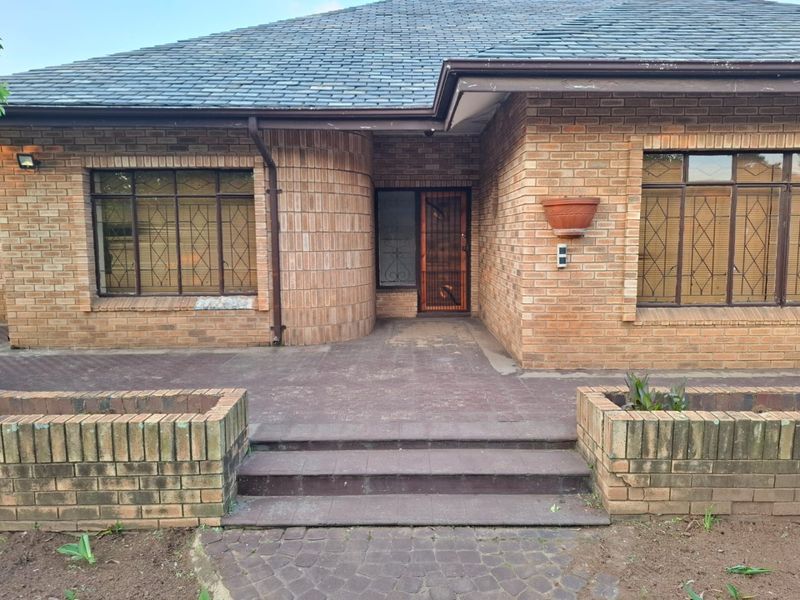 Front entrance of a face brick house featuring a tiled roof, security gates, and paved approach with integrated brick planters.