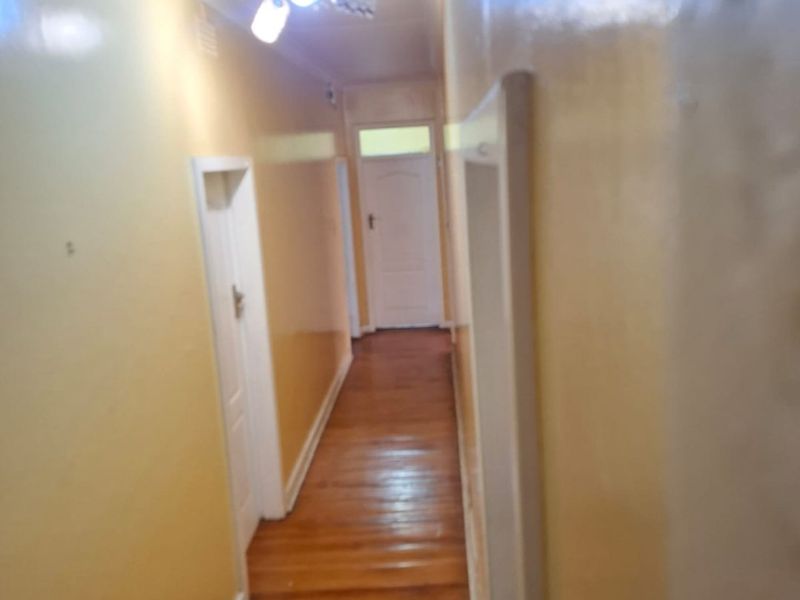 A narrow residential hallway featuring polished hardwood flooring and multiple internal doors, requiring cosmetic updates to the wall finishes.