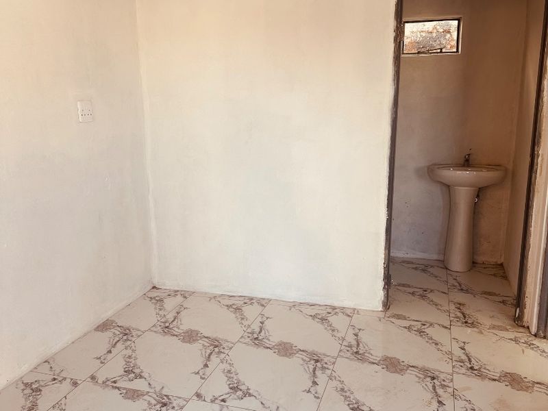 An empty bedroom featuring marble-look floor tiles and a small attached washroom area with a pedestal basin.