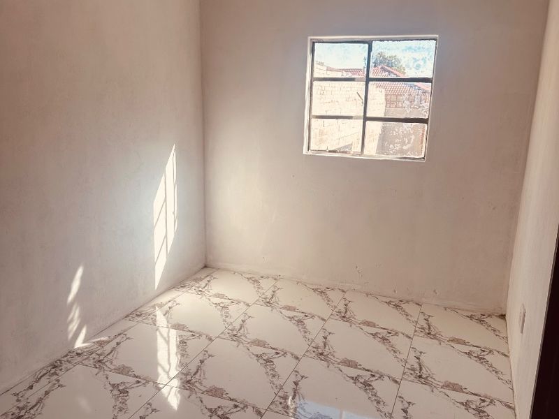 An empty bedroom featuring marble-look tiled flooring, white walls with ceiling cornice, and a single metal-framed window.