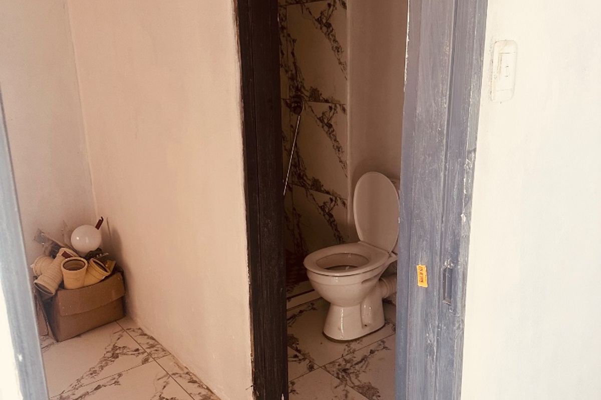 A small bathroom featuring marble-look floor and wall tiles, currently in an unfinished state with exposed door frames and incomplete finishes.