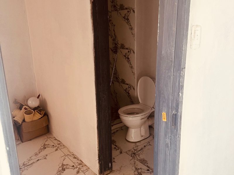 A small bathroom featuring marble-look floor and wall tiles, currently in an unfinished state with exposed door frames and incomplete finishes.