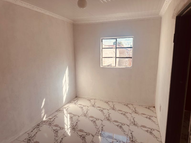 An empty bedroom featuring tiled flooring, decorative ceiling cornicing, and a steel-framed window, awaiting final finishes and personal touches.