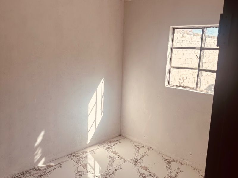 A bright, empty bedroom featuring modern patterned floor tiles, decorative ceiling cornicing, and a metal-framed window.