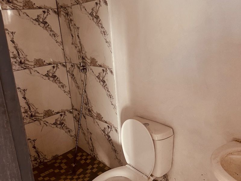 A compact bathroom featuring a shower enclosure, toilet, and wall-mounted basin, requiring cosmetic updates and finishing to improve its overall condition.