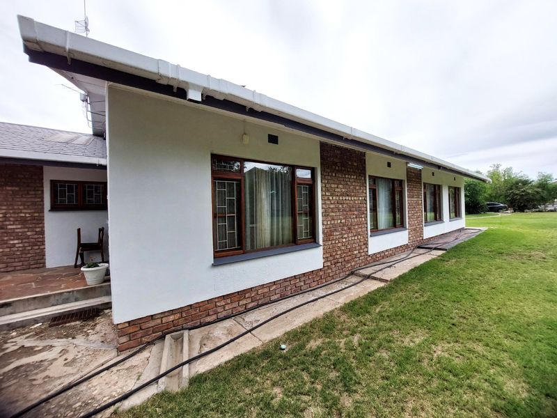 Rear view of the house featuring a combination of brick and plastered walls, timber-framed windows with security bars, and a concrete patio area.