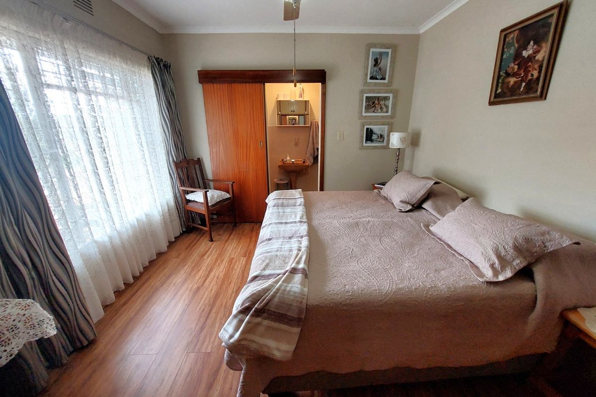 A well-lit bedroom featuring laminate flooring, a ceiling fan, and direct access to an en-suite bathroom through a sliding door.