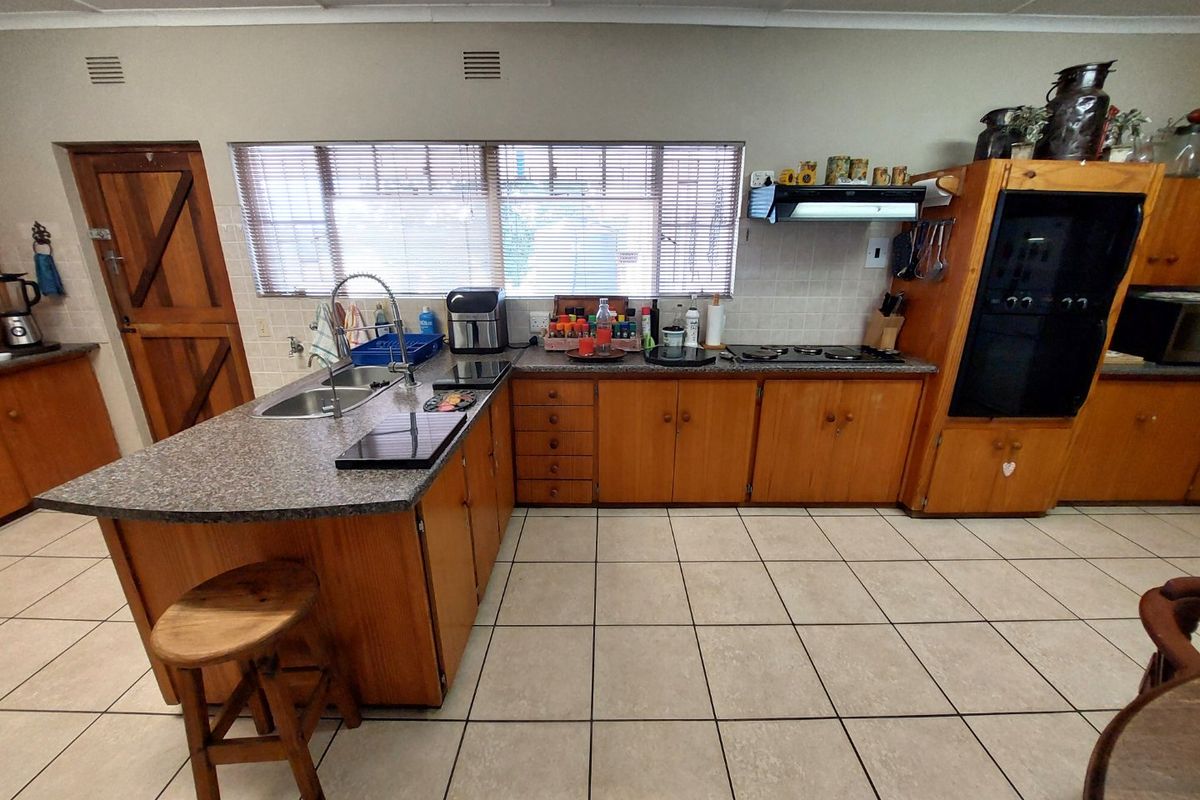 Functional kitchen featuring wooden cabinetry, granite countertops, built-in oven, hob, and extractor fan, with tiled flooring and natural light from a large window.