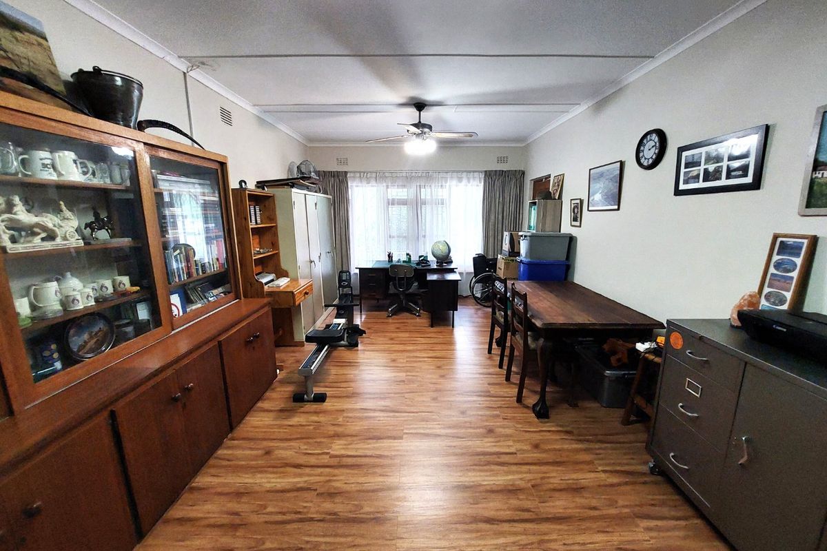 A spacious living area featuring laminate flooring, a ceiling fan, and coved cornicing, offering a versatile layout for various living or office configurations.