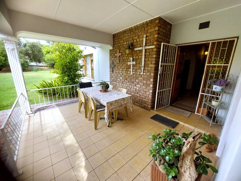 A covered patio area featuring tiled flooring, an exposed brick feature wall, and direct access to the garden and main entrance.