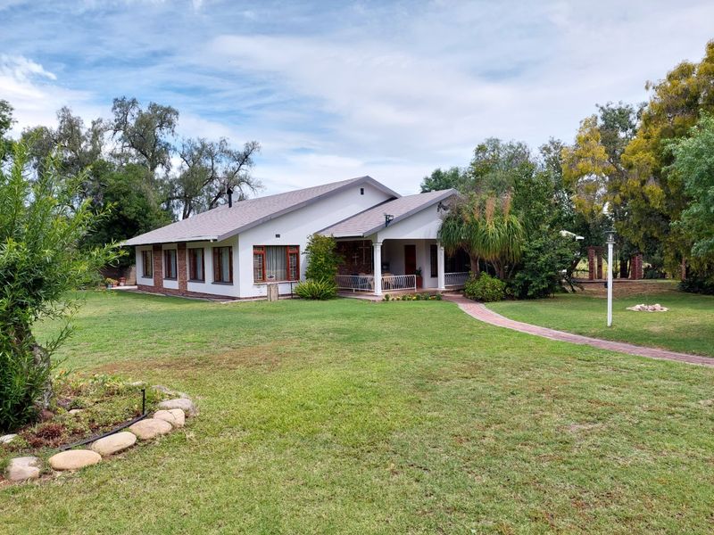 A well-maintained single-story house featuring a tiled roof, brick and plaster facade, and a covered patio set within a spacious landscaped garden.