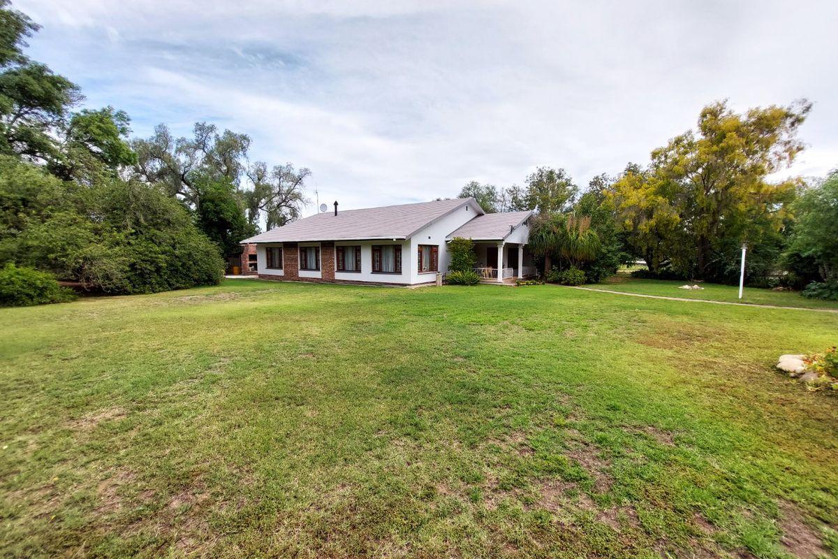A spacious rear view of the house featuring a large, well-maintained lawn, mature garden surroundings, and a covered patio area.