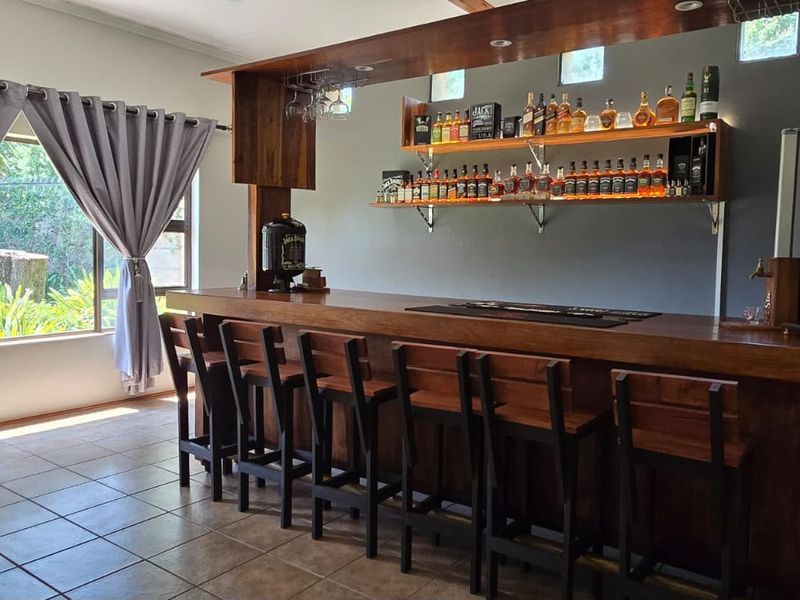 A well-appointed home bar area featuring a custom wooden counter, integrated shelving, and large windows overlooking the garden.