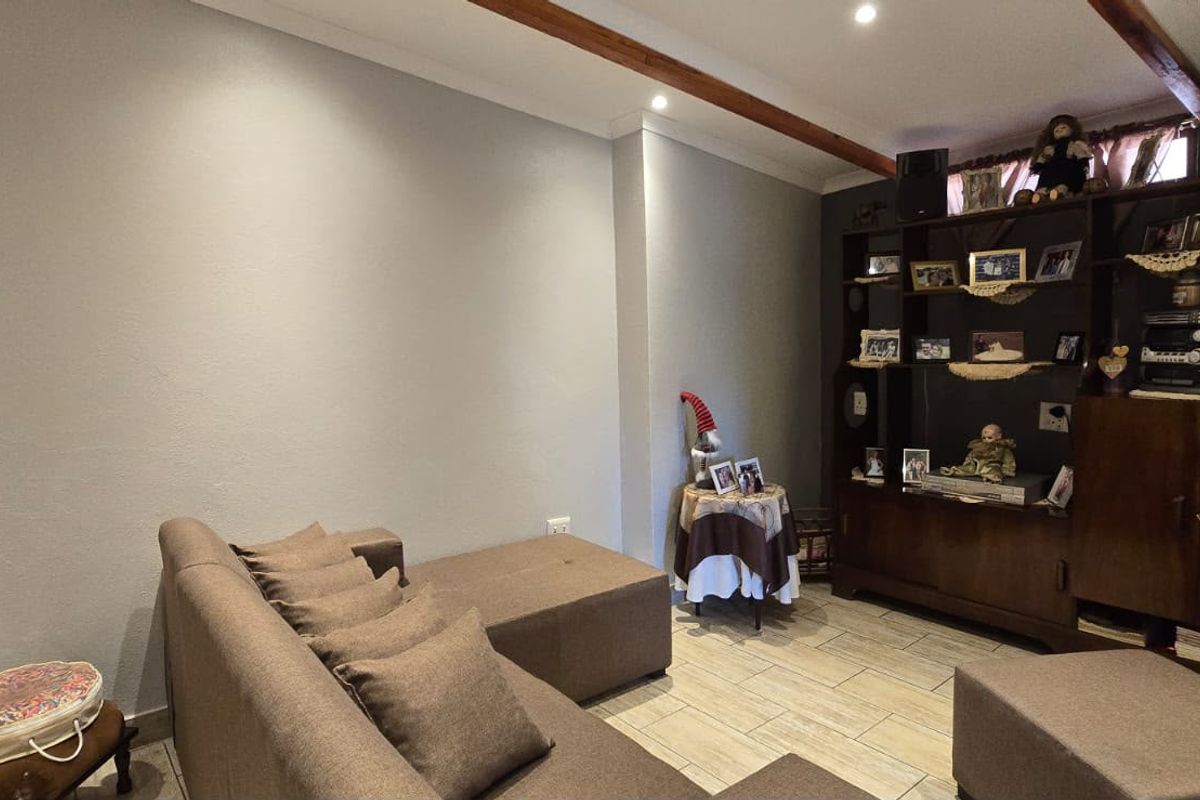 A cozy living room featuring exposed timber ceiling beams, tiled flooring, and recessed downlighting, offering a comfortable and functional space.
