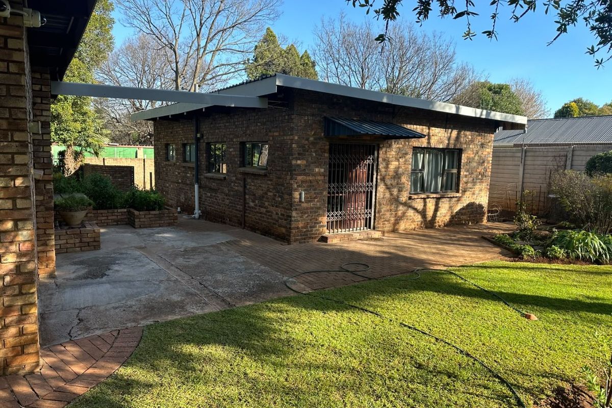 Rear view of a face brick outbuilding featuring a paved patio area, security gate, and established garden surroundings.