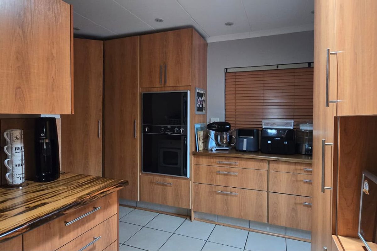A functional kitchen featuring wood-look cabinetry, built-in oven, tiled flooring, and ample storage space with a warm, traditional aesthetic.