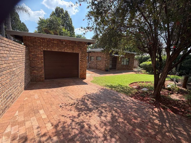 A well-maintained front exterior view featuring a brick driveway, a single garage with a roll-up door, and a neat garden area.