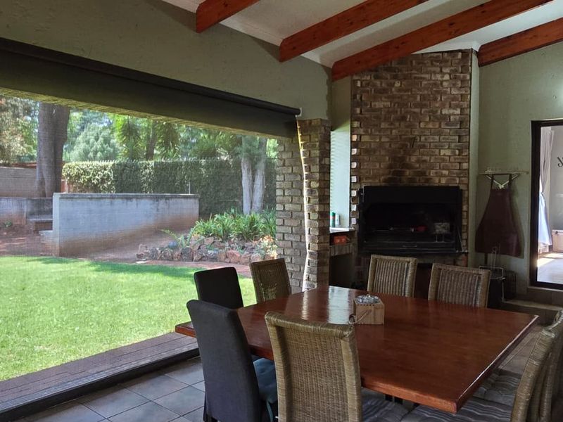 Covered patio area featuring a built-in braai, exposed timber ceiling beams, and direct access to the garden through large sliding doors.