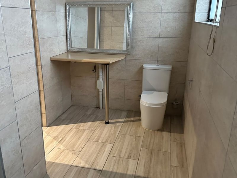 A clean, neutral-toned bathroom featuring floor-to-ceiling tiling, a modern toilet, and a wall-mounted vanity shelf.