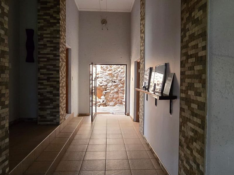 A spacious hallway featuring tiled flooring and decorative stone-clad pillars, leading towards an exterior entrance.