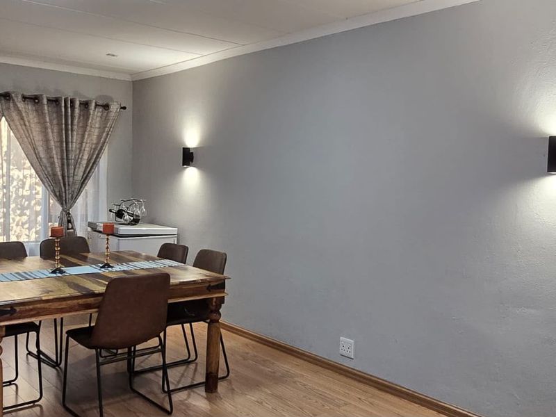 A well-lit dining room featuring laminate flooring, neutral grey walls, and modern wall-mounted lighting fixtures.