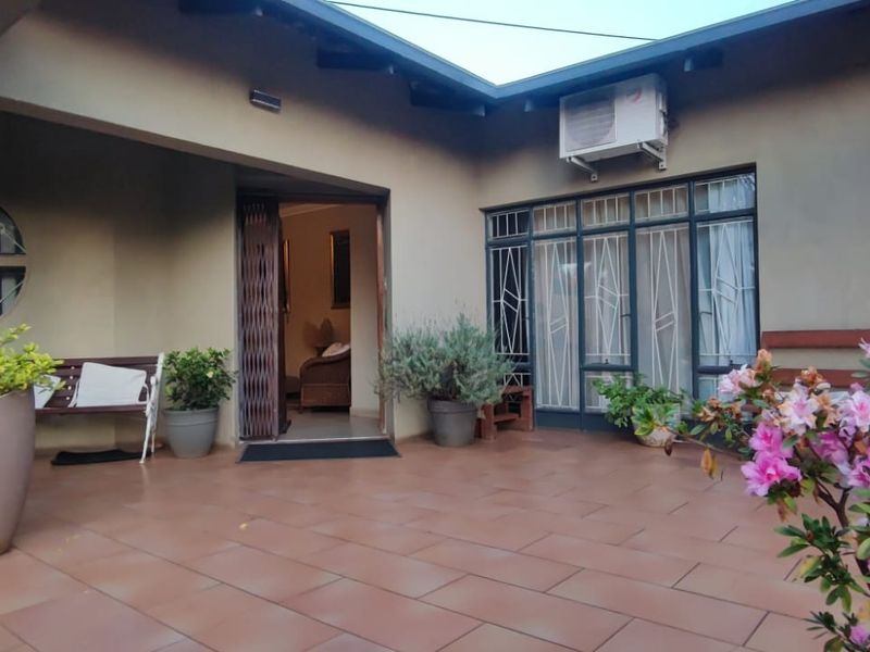 A covered patio area featuring tiled flooring, metal support columns, and direct access to the interior through a security gate and sliding glass doors.