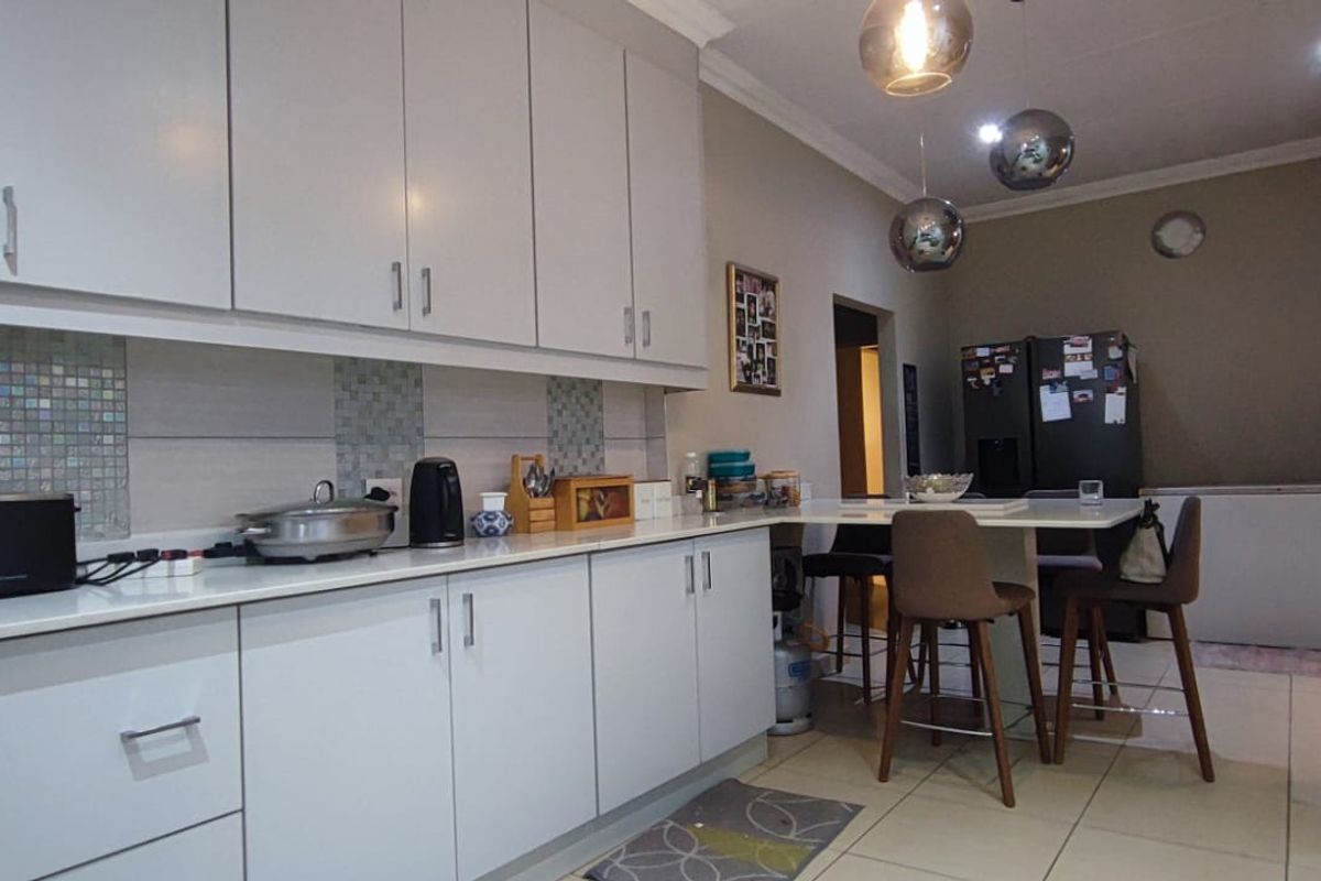 A functional kitchen featuring modern white cabinetry, a tiled backsplash, and an integrated breakfast bar area with contemporary pendant lighting.