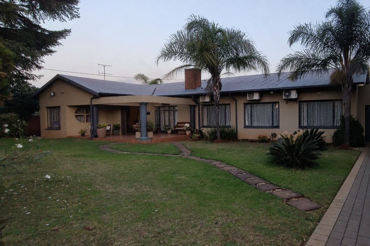 Rear view of the house featuring a covered patio, established garden, paved walkway, and exterior air conditioning units.