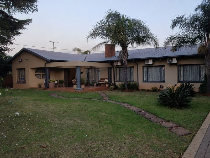 Rear view of the house featuring a covered patio, established garden, paved walkway, and exterior air conditioning units.