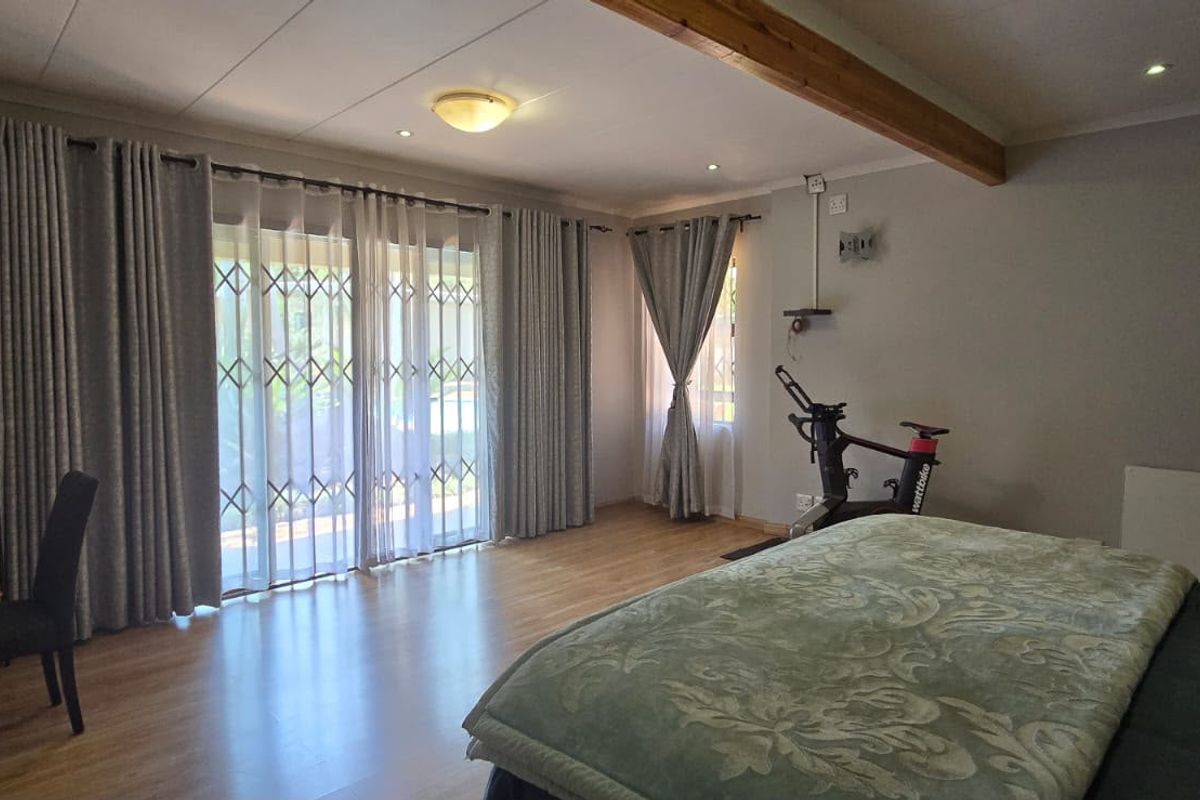 Spacious bedroom featuring laminate flooring, an exposed timber ceiling beam, and a sliding glass door with security gate providing access to the outdoors.